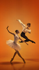 Ballet dancers captured in dramatic jump and poised stance on vivid orange background. Concept of...