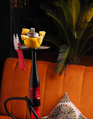 Hookah with lemon and scissors placed on an orange sofa in a cozy lounge