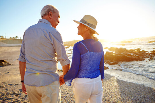 Holding hands, back and mature couple on beach for vacation, getaway or holiday in summer together. Sunset, love and man with woman by ocean for connection in marriage on romantic weekend trip.