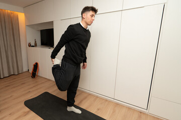 Young man stretching quadriceps on yoga mat at home