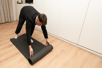 Man rolling up yoga mat after home workout