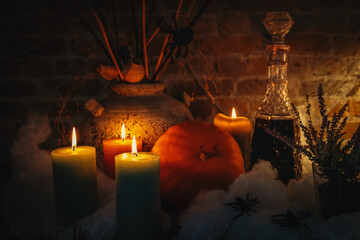 Halloween still life with burning candles, pumpkin, vintage pottery and spooky decorations. Warm moody lighting creates a cozy autumn atmosphere.
