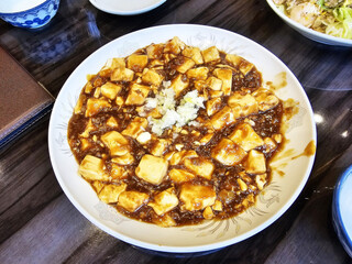 Mapo tofu garnished with green onions in a white bowl, traditional Chinese Sichuan dish.
