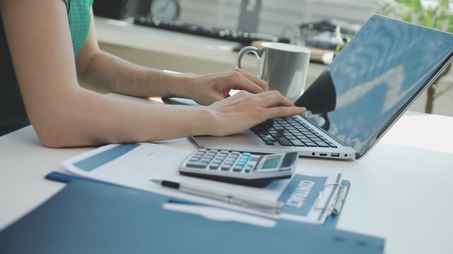 Two financial accountants analysing business spreadsheets on laptop computer, sitting at office desk, looking through paper documents, using calculator working with databases, checking excel tables