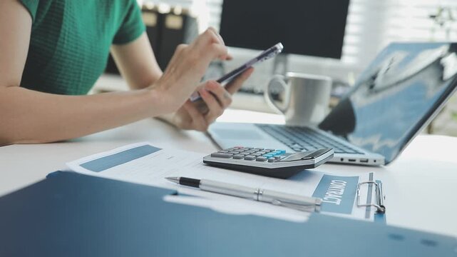 Two financial accountants analysing business spreadsheets on laptop computer, sitting at office desk, looking through paper documents, using calculator working with databases, checking excel tables