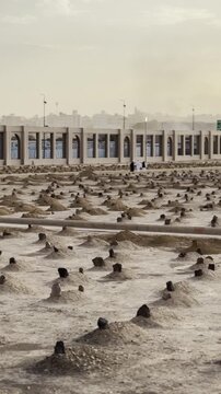 Atmospheric sunset shot of the sacred Jannat al-Baqi cemetery, capturing ancient earth-mound graves, soft desert light and a spiritual ambiance beneath a hazy sky, honoring Islamic historical figures.