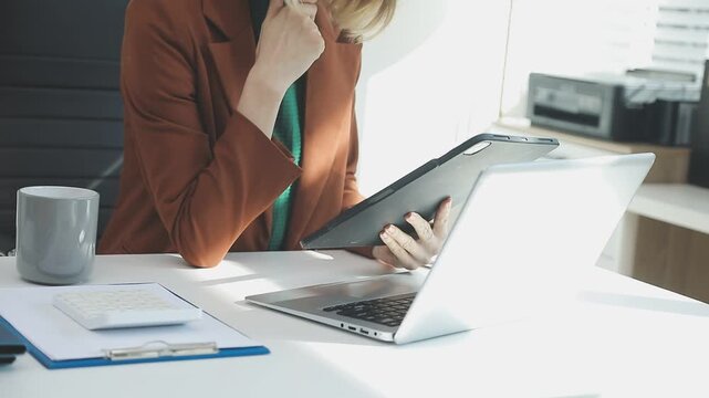 Two financial accountants analysing business spreadsheets on laptop computer, sitting at office desk, looking through paper documents, using calculator working with databases, checking excel tables