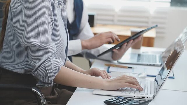 Two financial accountants analysing business spreadsheets on laptop computer, sitting at office desk, looking through paper documents, using calculator working with databases, checking excel tables