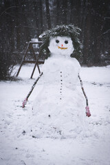 Cheerful snowman in a snowy garden with fir branches and gloves.