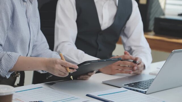 Two financial accountants analysing business spreadsheets on laptop computer, sitting at office desk, looking through paper documents, using calculator working with databases, checking excel tables