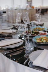 Elegant banquet table setting with crystal glasses, appetizers, and plates on a reflective black surface