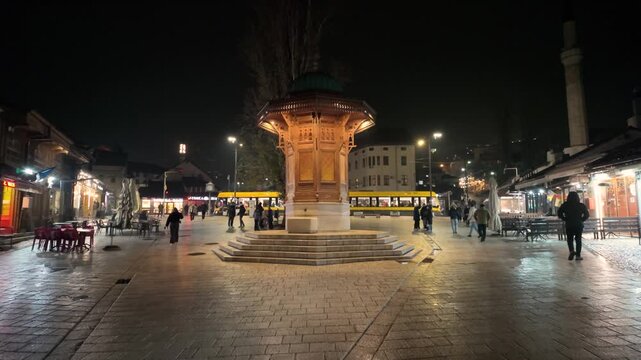 Sarajevo, Bosnia and Herzegovina &ndash; December 2 2025: The Sebilj fountain on Bascarsija square is seen at night in slow motion with people walking through the area