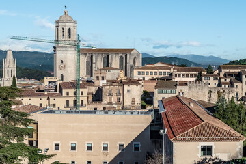 Panoramic view of Girona Cathedral rising above the city, with a construction crane nearby and the Pyrenees in the background. Historic buildings of Girona, Catalonia create a classic medieval skyline