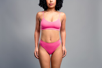 Young confident woman in pink bikini standing against grey background showcasing body positivity...