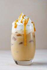 Iced caramel latte coffee in a glass with whipped cream and syrup drizzle. Cold summer frappuccino drink with ice cubes on light background.