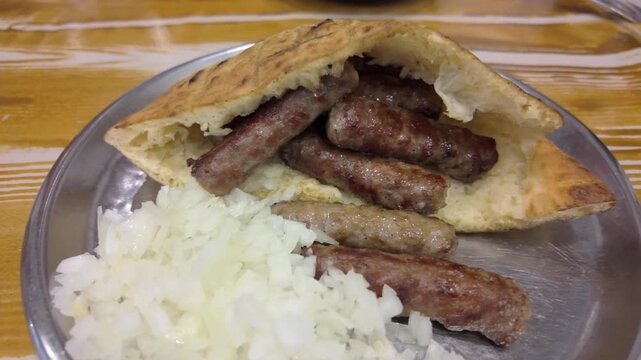 Close-up video of cevapi served in lepinja with onions as the camera moves right, showing texture and traditional Balkan food details