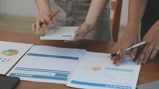 Two financial accountants analysing business spreadsheets on laptop computer, sitting at office desk, looking through paper documents, using calculator working with databases, checking excel tables