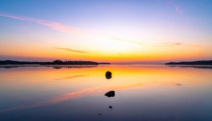 A tranquil landscape scene featuring a lake reflecting the vibrant colors of a sunset sky, with rocks in the foreground and a distant shoreline.