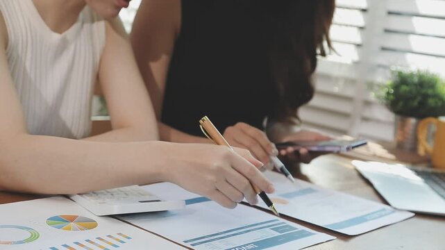 Two financial accountants analysing business spreadsheets on laptop computer, sitting at office desk, looking through paper documents, using calculator working with databases, checking excel tables