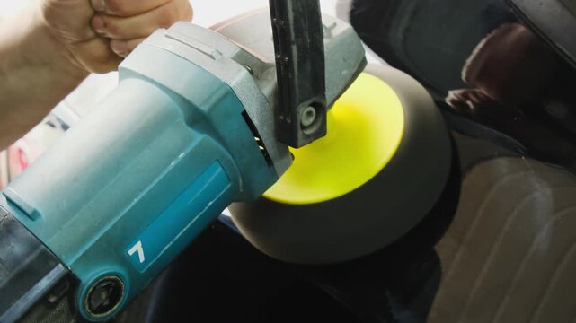 Service technician polishes car body holding tool in hands. Male master eliminates small unevenness and modifies material in workshop