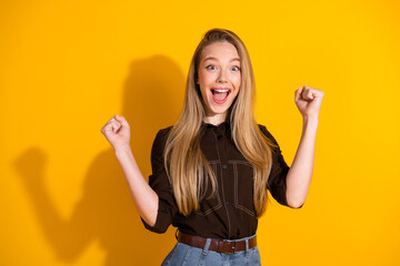 Young woman celebrating success in a casual stylish outfit with a bright yellow background and a...