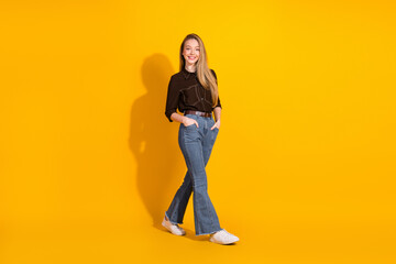 Young woman in casual stylish outfit walking against a bright yellow background smiling with...