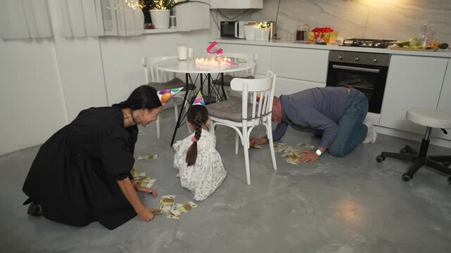 Birthday Party Cleanup Family Kitchen Floor: Adults and child clean confetti after celebration.