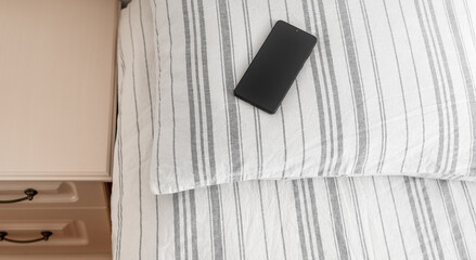 Smartphone on a striped pillow next to a bedside table