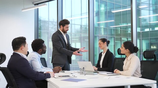 Male CEO praises female employee for excellent job during meeting in boardroom. Happy diverse team of co-workers support colleague with applause, clapping hands, celebrate success and great results