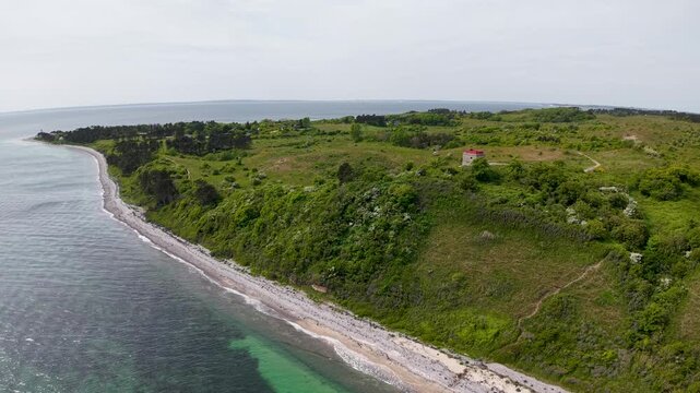 Drone shot along a lush green coastal cliff and turquoise sea in Denmark, showing verdant fields above the shoreline.