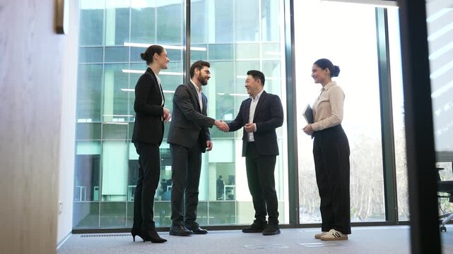 Meeting of group business people shaking hands in lobby of modern business center. Professional diverse men and women exchanging partner handshake standing in glass office. Collaboration and teamwork