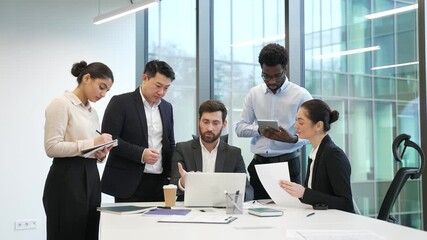 Male boss with group of diverse employees discussing work issues using laptop at meeting in office. Manager explains details of project development to subordinates, gives tasks, engaging in teamwork - Powered by Adobe