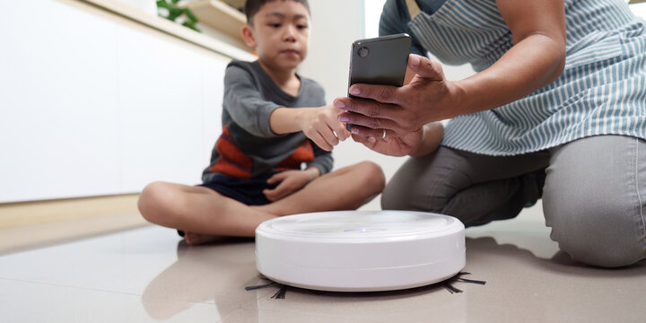Father and son engaging with smart home device. Controlling robot vacuum with smartphone.