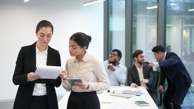 Group of male employees whispering behind two female coworkers in office. Colleagues gossiping and mocking in background of women. Problem of bullying, mobbing, women's rights and sexism in workspace