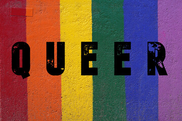 QUEER. Word written on a wall painted with the colors of the rainbow flag.