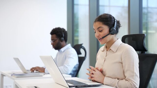 Two corporate operators working in customer support service on helpline telesale using laptop. Team of call center agents in headsets, men and women helping online, answer questions sitting in office