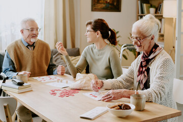 Senior Caucasian man and senior Caucasian woman sitting at table playing board game with young adult Caucasian woman, all interacting and engaging with game pieces together