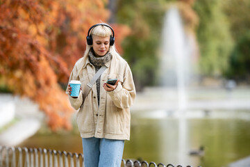 Young woman walking, listening to music on smartphone in autumn park