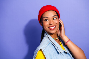 Young woman with red beanie smiling in denim vest against purple background looking stylish and...