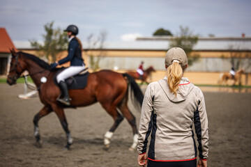 Horse trainer supervising rider during equestrian training in paddock