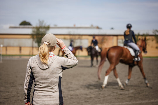 Horse trainer instructing riders  before equestrian jumping event. Woman animal instructor focused on horseback riding in paddock