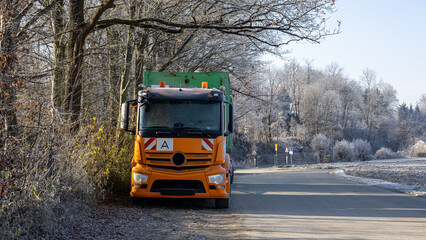 Front view of orange truck parked beside frosty trees on a rural road, depicting winter transport conditions and roadside infrastructure