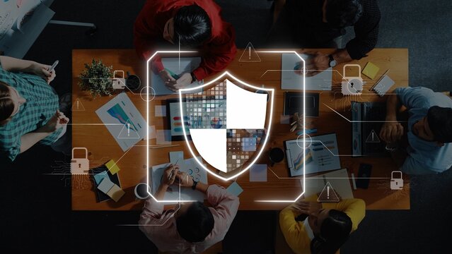 A diverse group of professionals engages in a collaborative meeting at a conference table while a digital shield symbol represents cybersecurity and protection. Raster