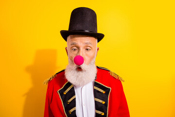 Clown magician in red ornate coat with pink nose and top hat on bright yellow background for circus show and holiday entertainment