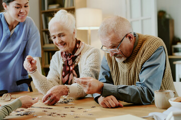 Senior Caucasian woman and senior Caucasian man assembling jigsaw puzzle together at table while...