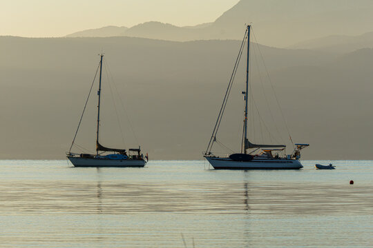 Two sailboats anchored on a calm lake at sunset with mountains in the background.