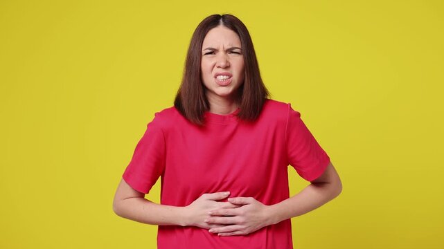 Sick ill sad tired young woman wear pink t-shirt casual clothes put hands on abdomen suffering from stomach-ache griping bellyache feel bad seedy isolated on plain yellow background. Lifestyle concept