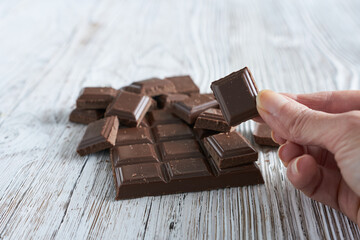Milk chocolate, confectionery. A piece of milk chocolate in a woman's hand, on a white wooden background.