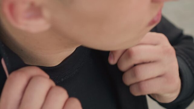 young man adjusting black hoodie collar and zipper closeup, hands fidget with fabric, fingers tugging sleeve and collar, urban casual outfit, subtle nervous energy, audition preparation vibe, textured