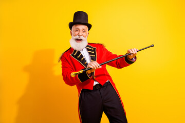 Obraz premium Cheerful elderly magician performs retro circus style tricks on bright yellow background in a vibrant red costume with cape and cane during holiday show